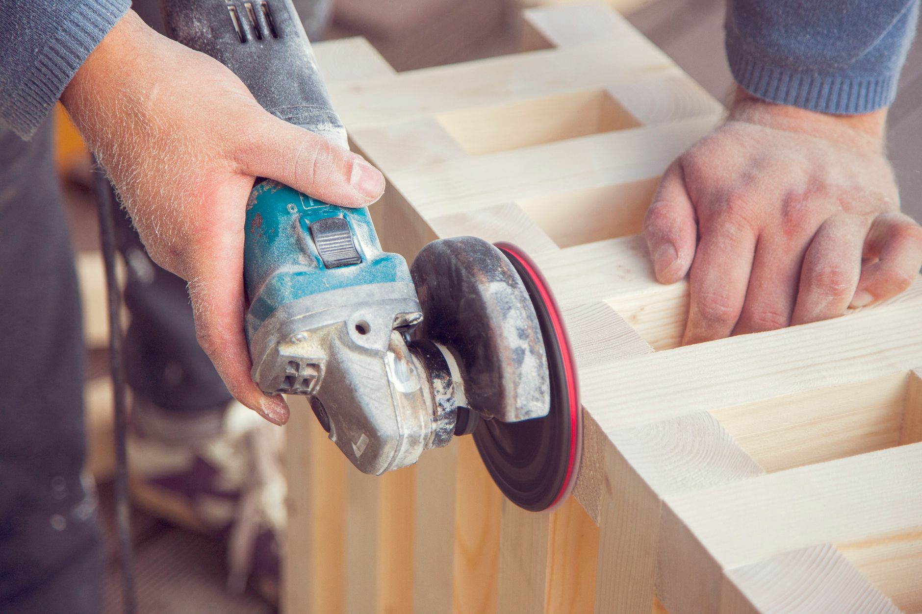 Carpenter using an angle grinder to finish a wood construction piece in a workshop